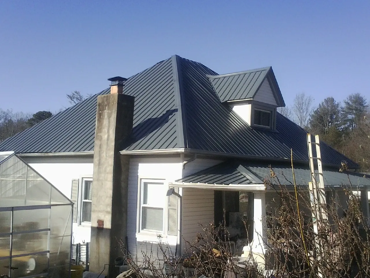 Dark blue standing seam metal roof on a white farmhouse with dormer — Slate & Tile Roof Repair by Roofing Brothers in East Bernard