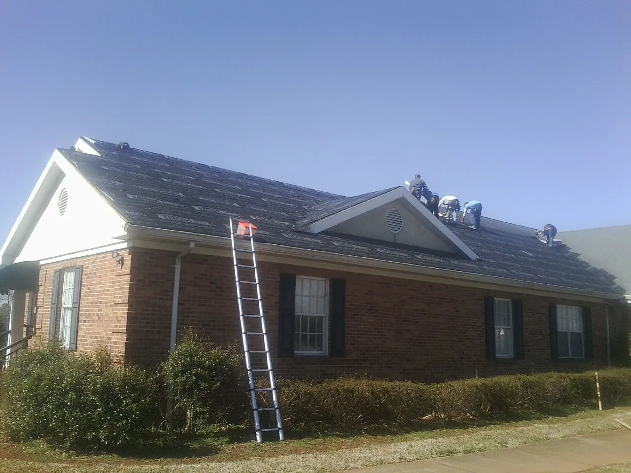 Crew tearing shingles off a brick ranch roof with a ladder set — Emergency Roof Repair work by our crew in East Bernard