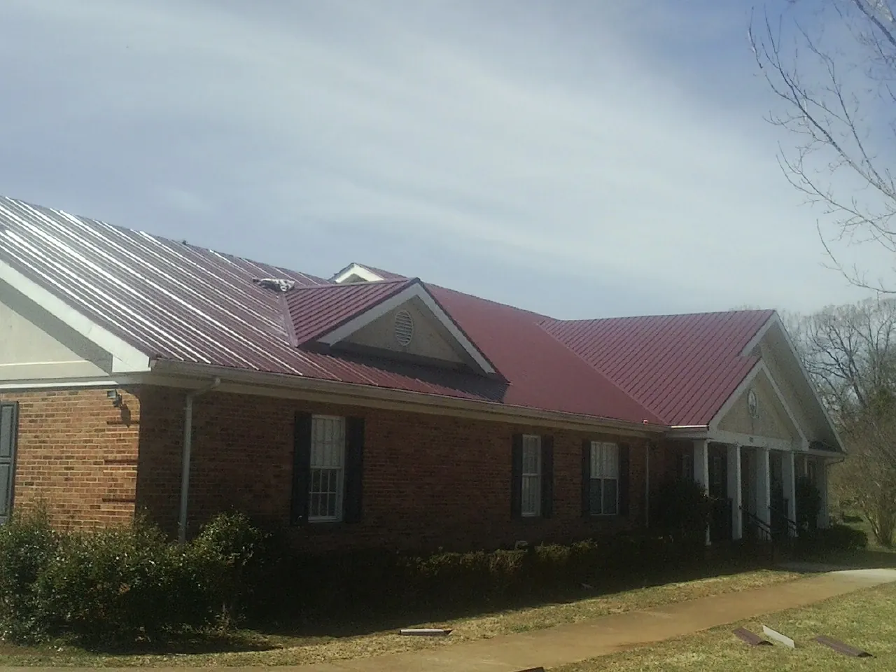 Red metal roof with gabled entries on a long brick building, from a Hail Damage Roof Repair job in East Bernard