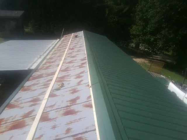 Old rusted panels beside newly installed green metal roofing — Wind Damage Roof Repair by Roofing Brothers in East Bernard