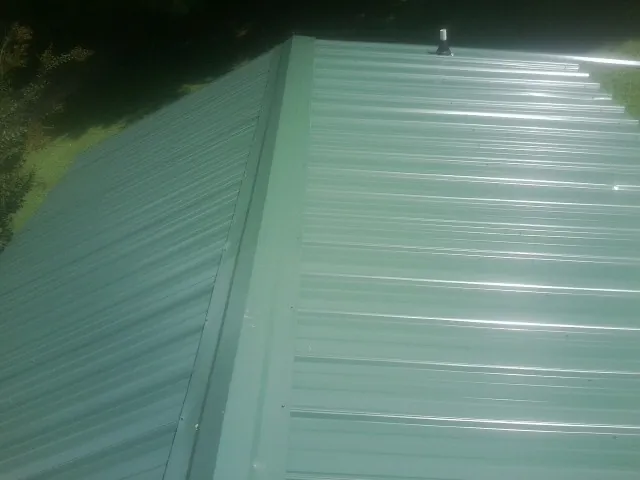 New green metal panels meeting at the ridge of a roof — Flat Roof Repair work by our crew in East Bernard