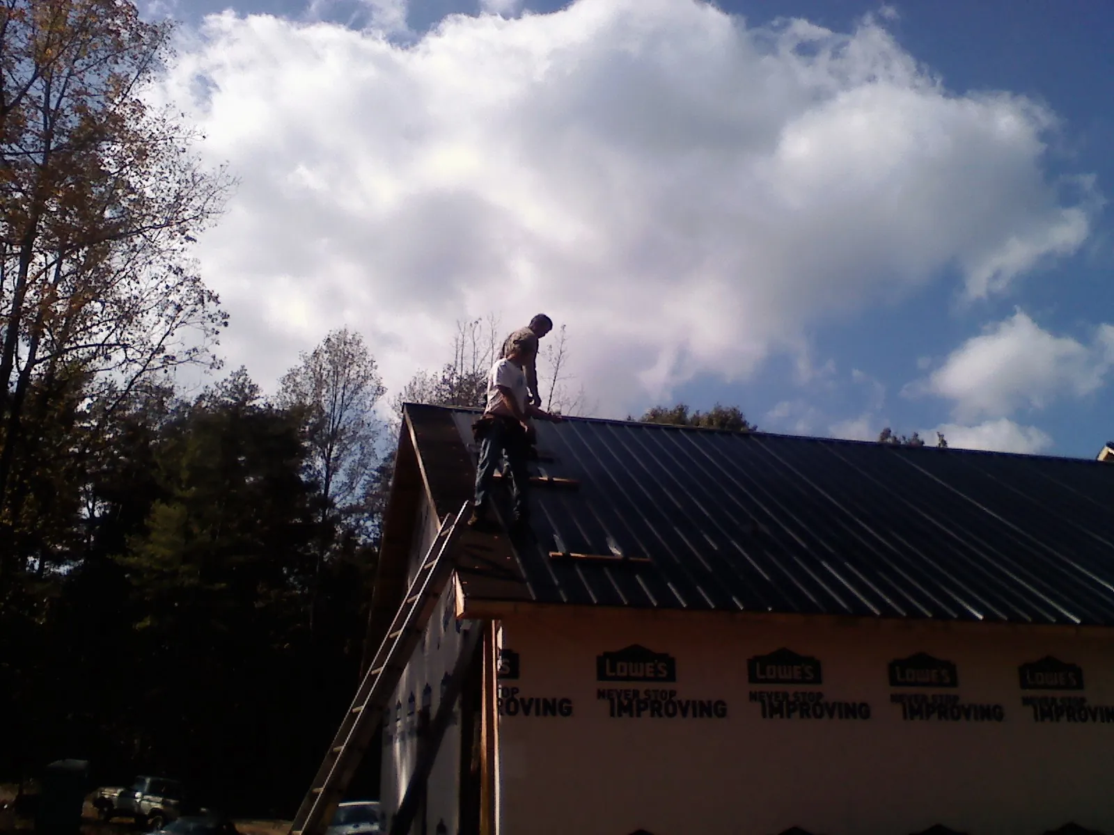 Roofer fastening dark metal panels high against a cloudy sky, from a Roof Inspection job in East Bernard
