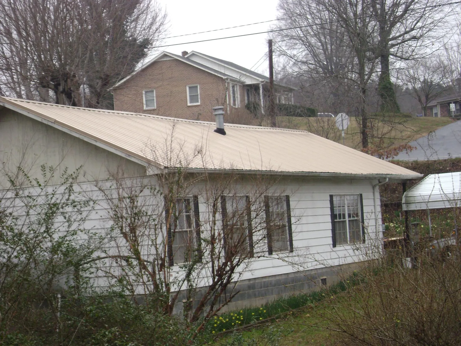 Tan metal roof on a white sided house set into a hillside — Commercial Roofing by Roofing Brothers in East Bernard