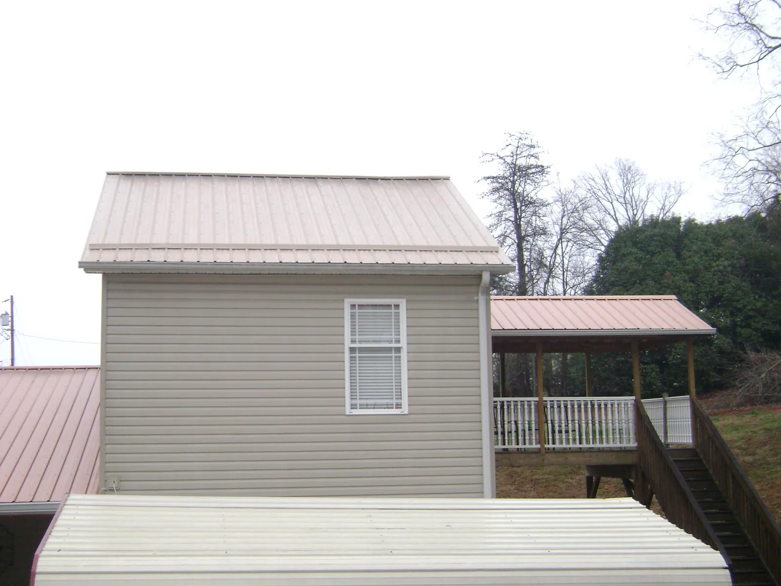 Tan metal roofs on a two story addition and attached porch, from a Roof Replacement job in East Bernard